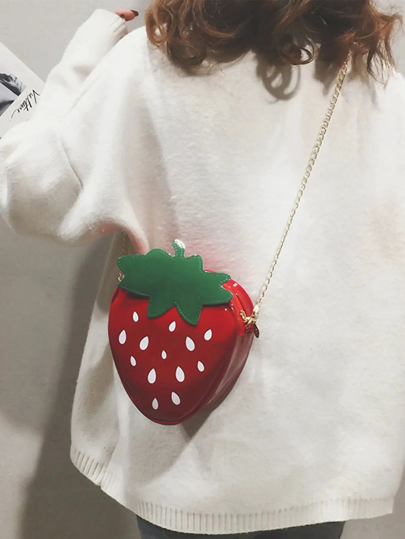 Strawberry-themed red crossbody bag with green leaf and white seed accents, gold chain strap