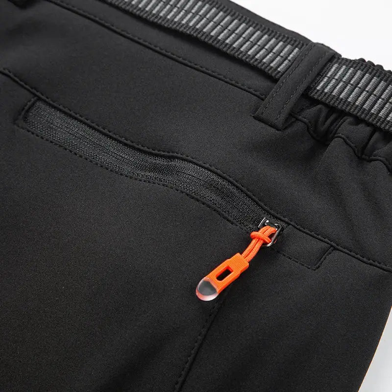 Men's black soft-shell hiking pants with orange zipper pull and elastic waistband