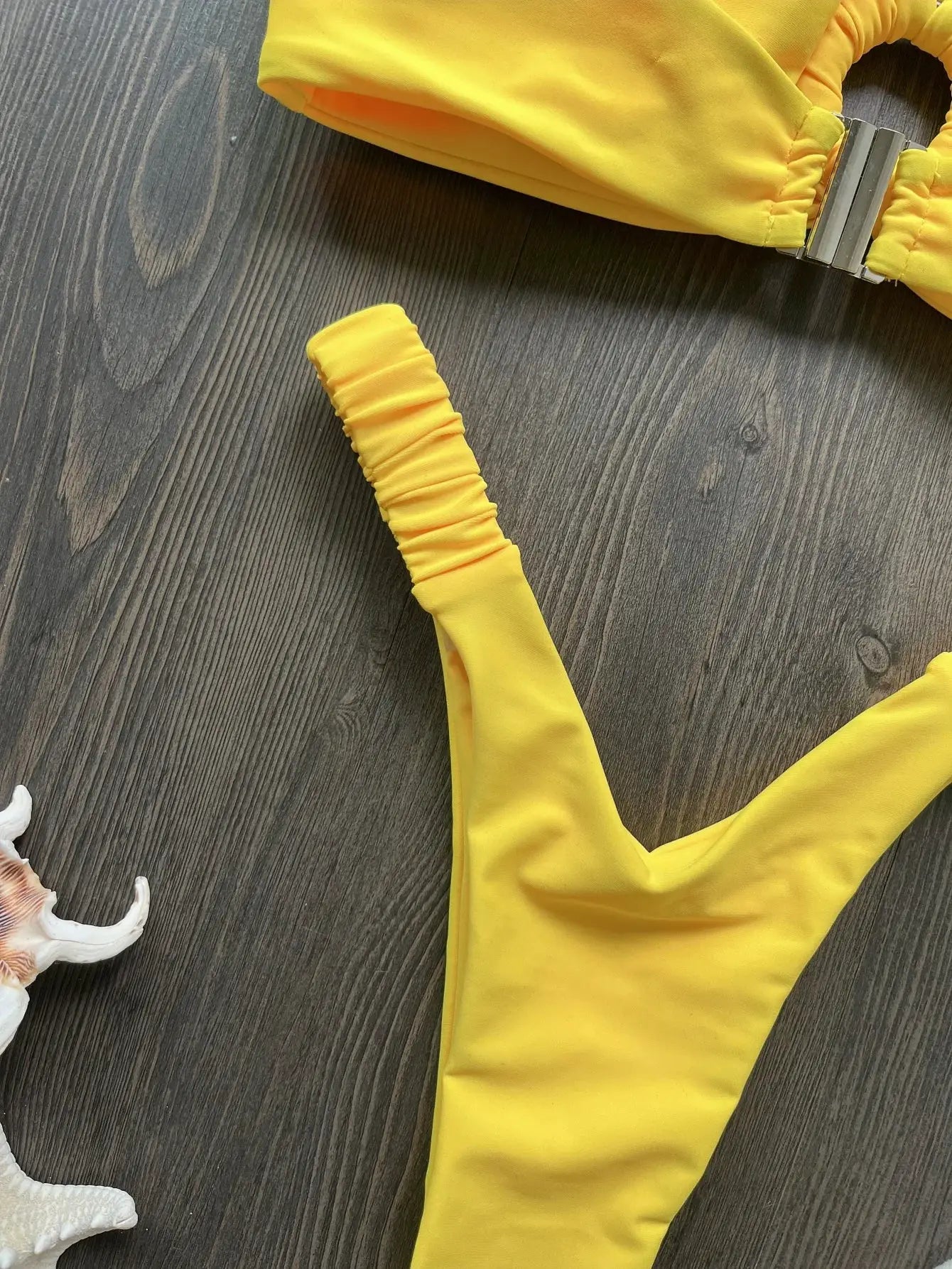 Yellow two-piece micro bikini set with ruched detailing and metal clasp, on dark wood background