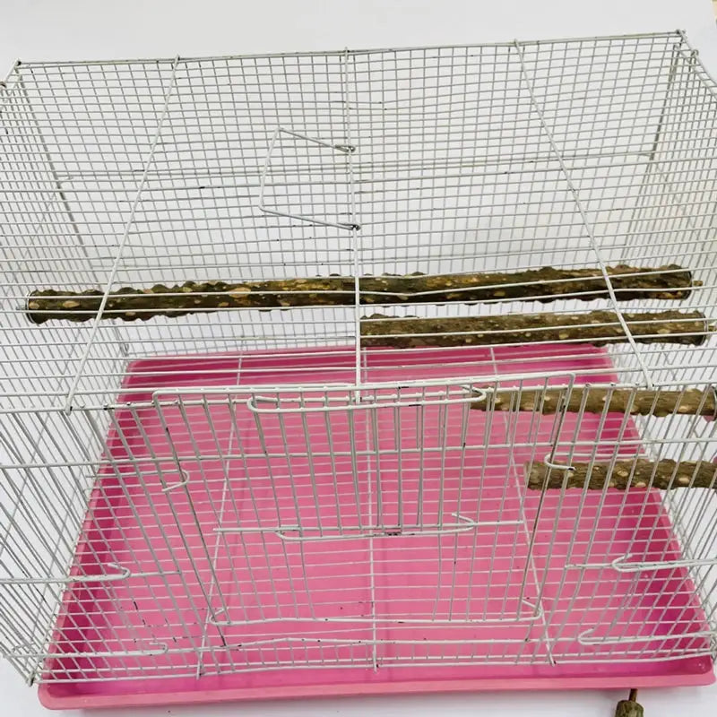 Bird claw-beak grinding bars and standing stick inside a metal bird cage with pink base tray