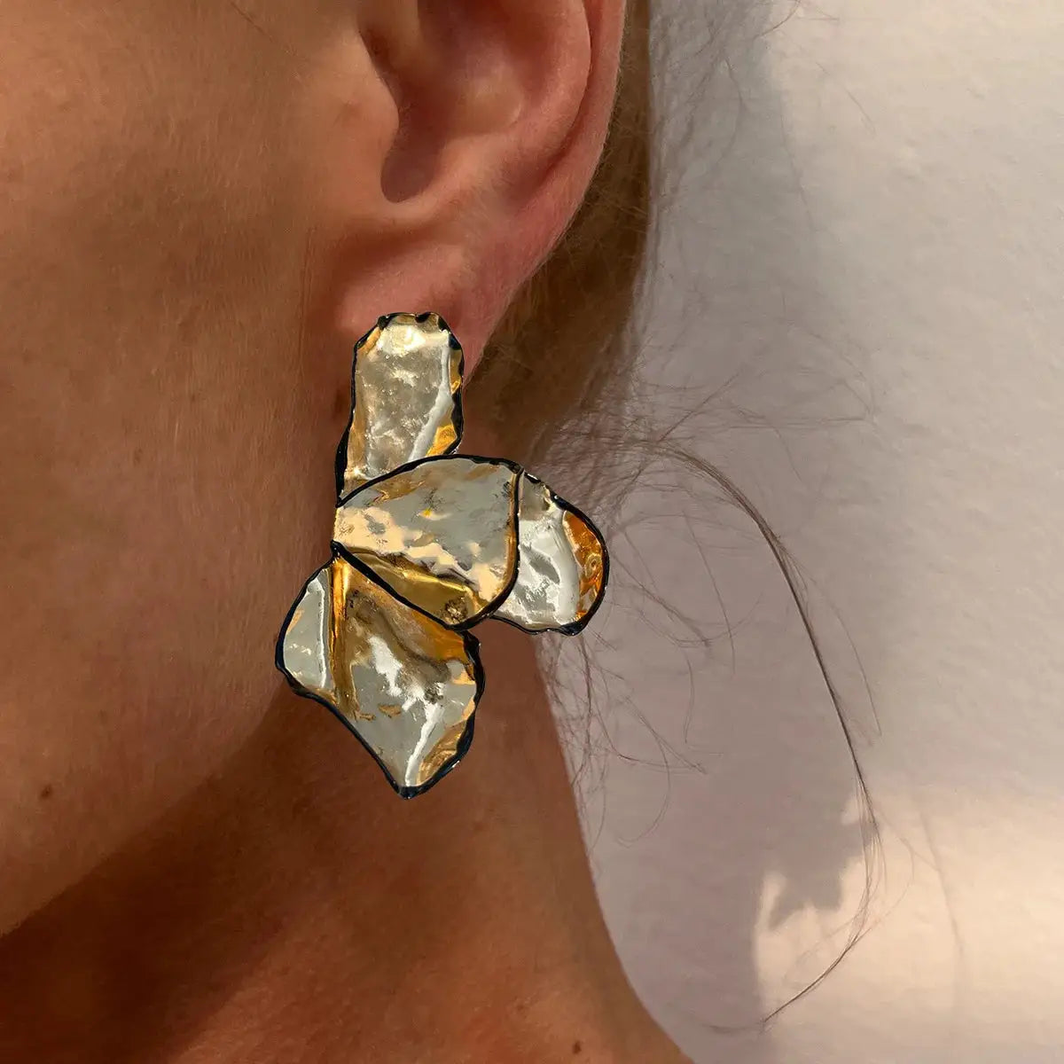 Earrings by Simples Market; metal irregular pleated petal design in gold and silver tones with black edges.