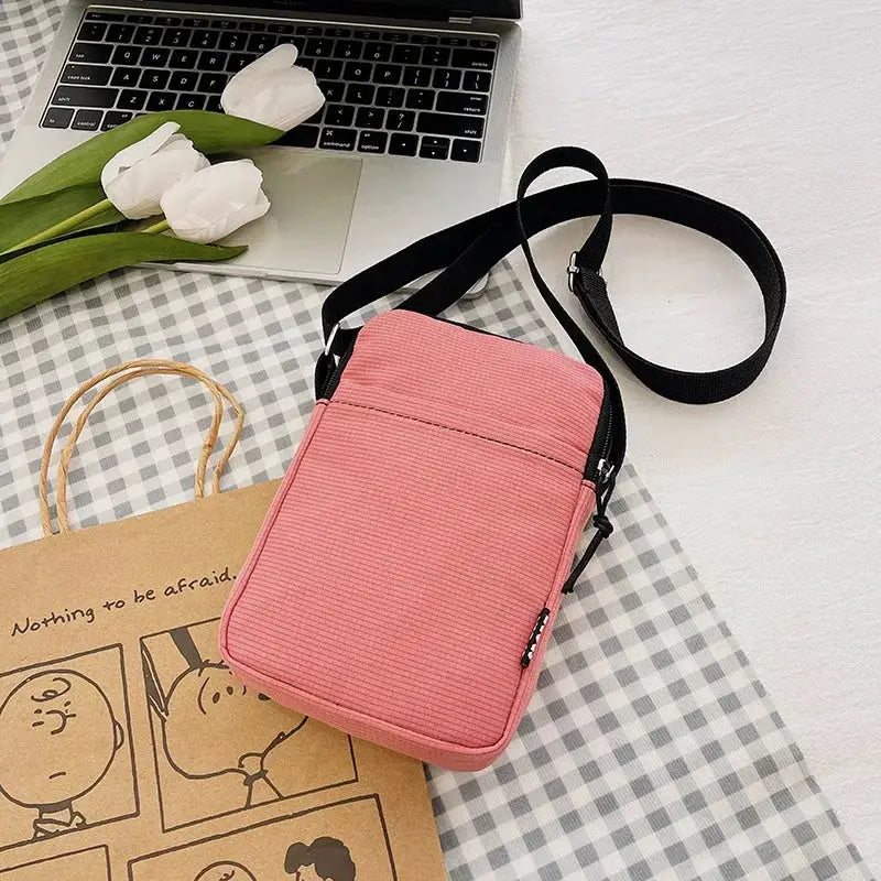 Pink vertical crossbody bag with black adjustable strap for phones and cards.
