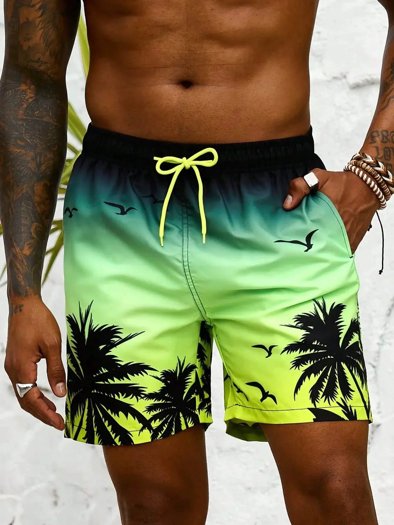 Board shorts by Simples Market, gradient green to teal with neon yellow drawstring and palm tree print.