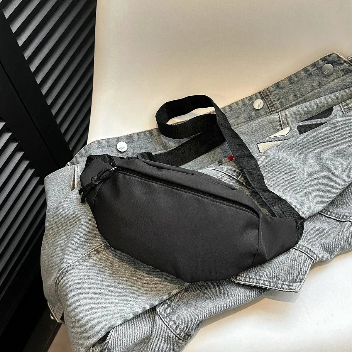 Fanny pack waist bag by Simples Market in black with adjustable strap, placed on a gray denim jacket.