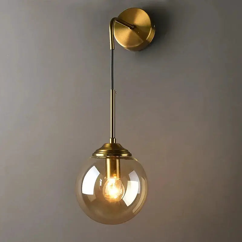 Modern glass wall lamp in golden brass with round clear globe shade