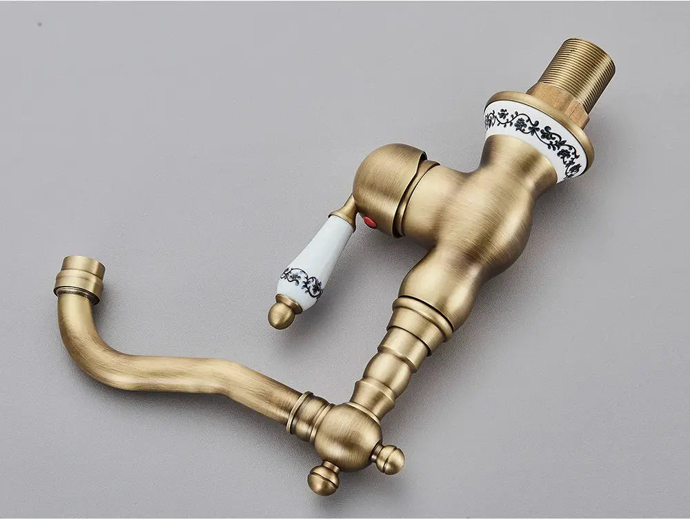 Antique brass bathroom faucet with rotating spout and white ceramic handle