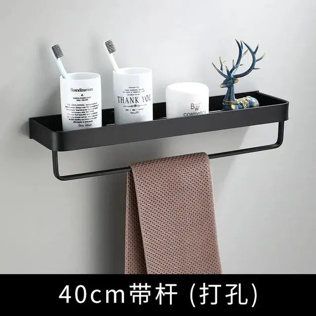 Wall-mounted black aluminum bathroom shelf with towel bar; holds white containers, a deer figurine, and a brown towel.