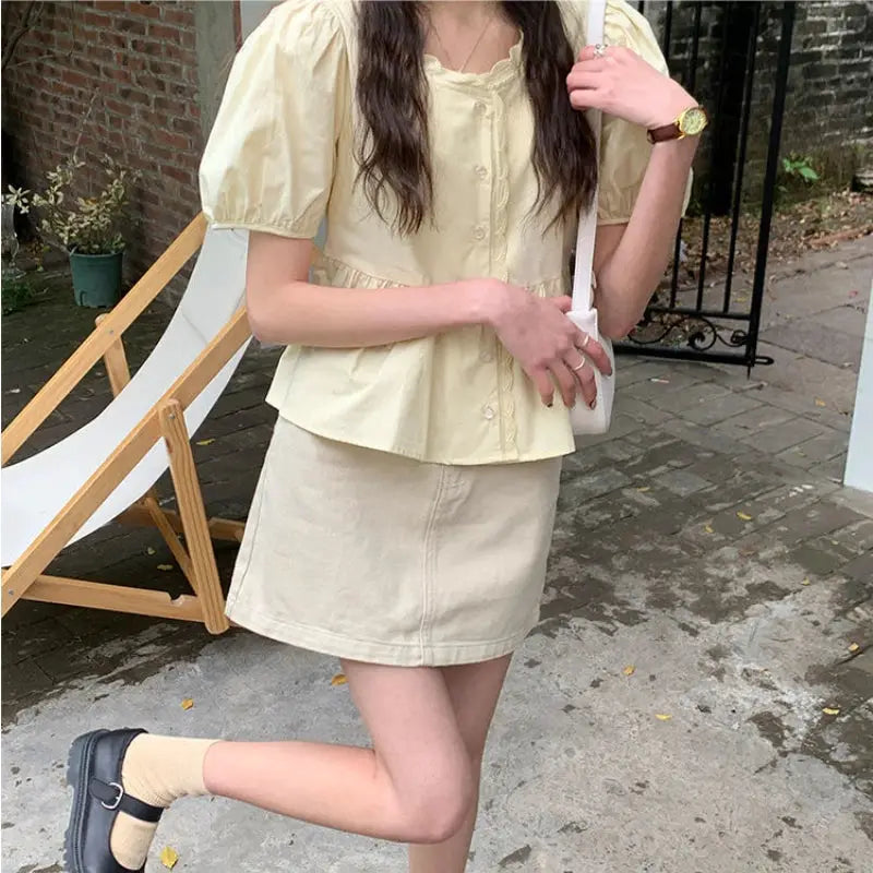 Women's pale-yellow short puff-sleeve peplum blouse with button front, paired with a beige mini skirt.