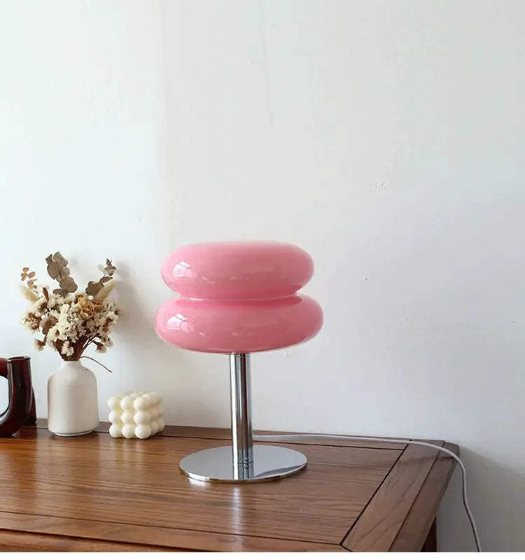 Macaron glass table lamp, pink double-donut shade with chrome base on a wooden table