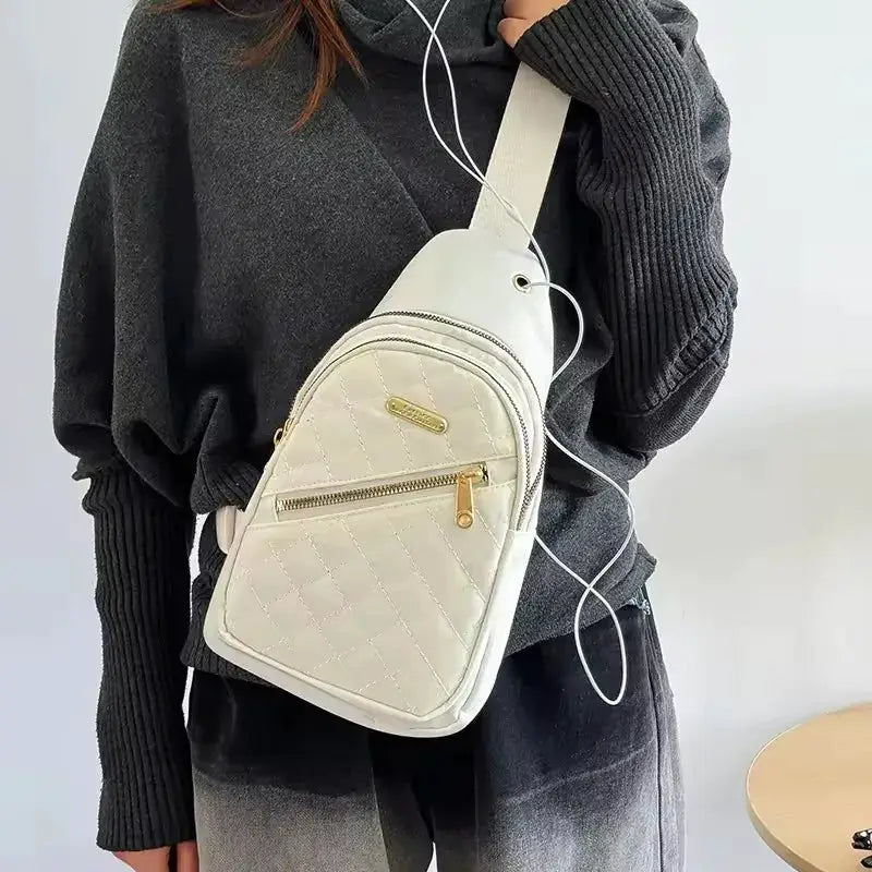 Minimalist cream quilted chest bag with front zip pocket and gold zipper pull, worn crossbody.