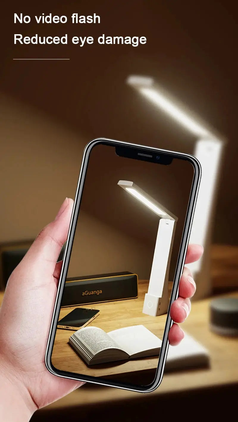 LED desk lamp, white foldable design with eye-protection lighting, shown on a wooden desk beside a book and smartphone