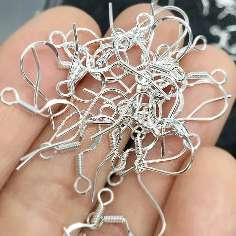 Silver 925 sterling ear wire hooks for jewelry making; hypoallergenic fish hooks in a pile.