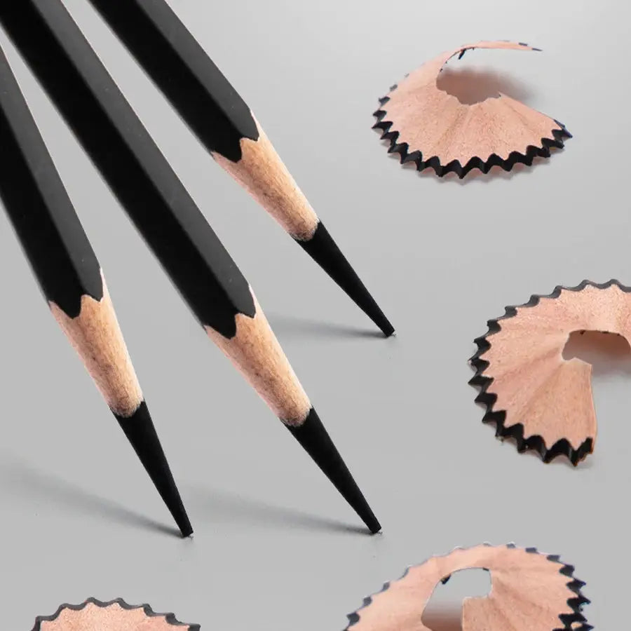 Professional graphite pencil set with three black sharpened pencils and wood tips on a gray surface with shavings.