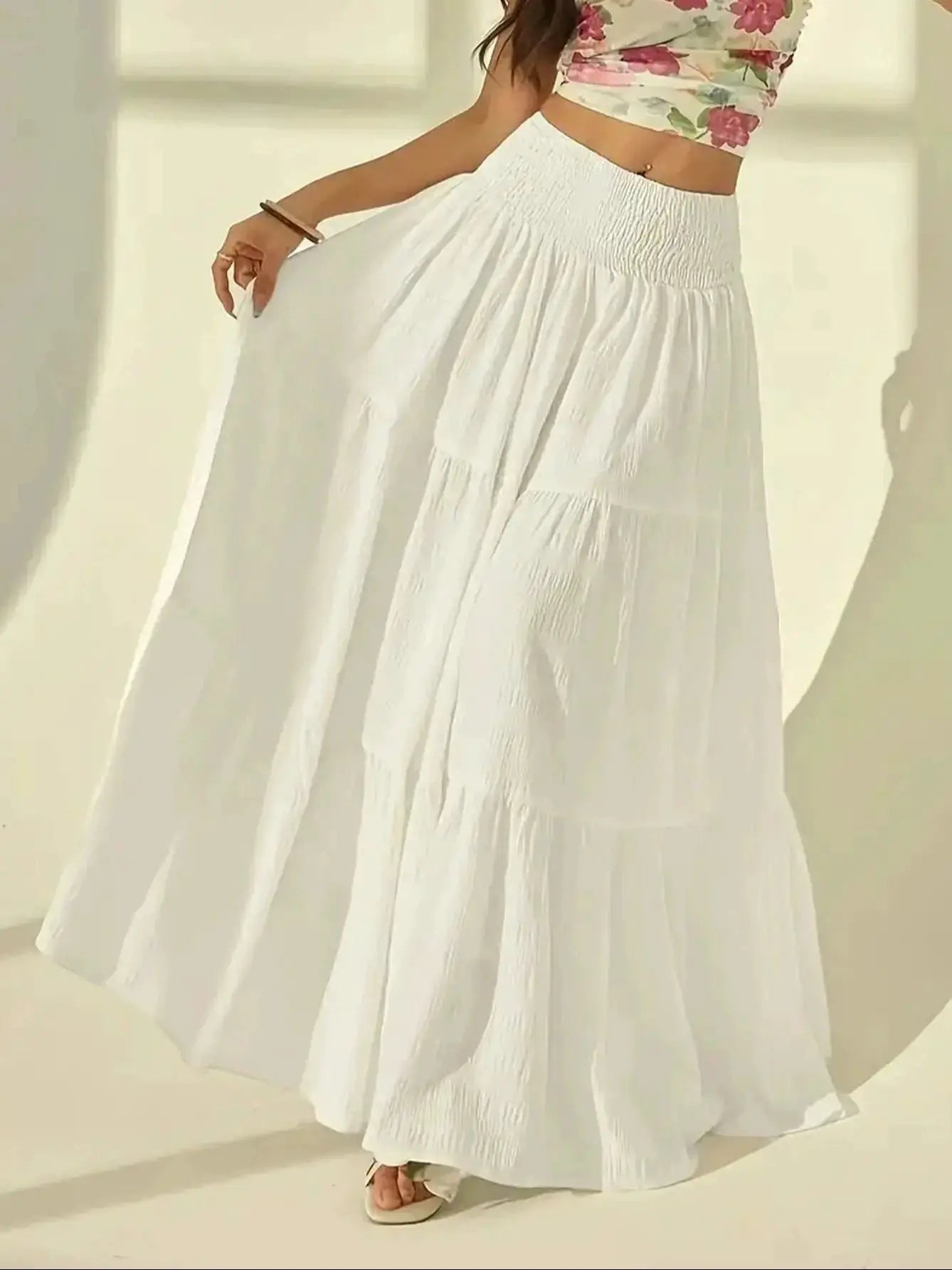 White tiered maxi skirt with high-waisted elastic waistband, flowing pleated silhouette.
