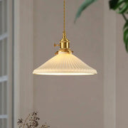 Pendant light with brass hardware and ribbed white shade, hanging in living room.