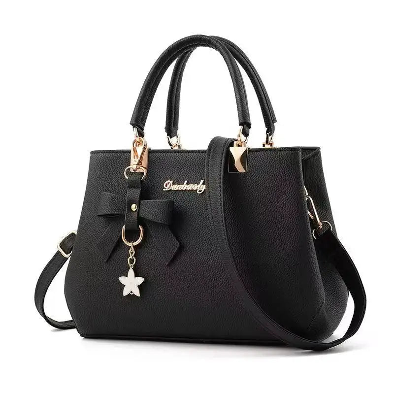 Black pebbled leather handbag with two top handles, bow charm, and gold hardware.