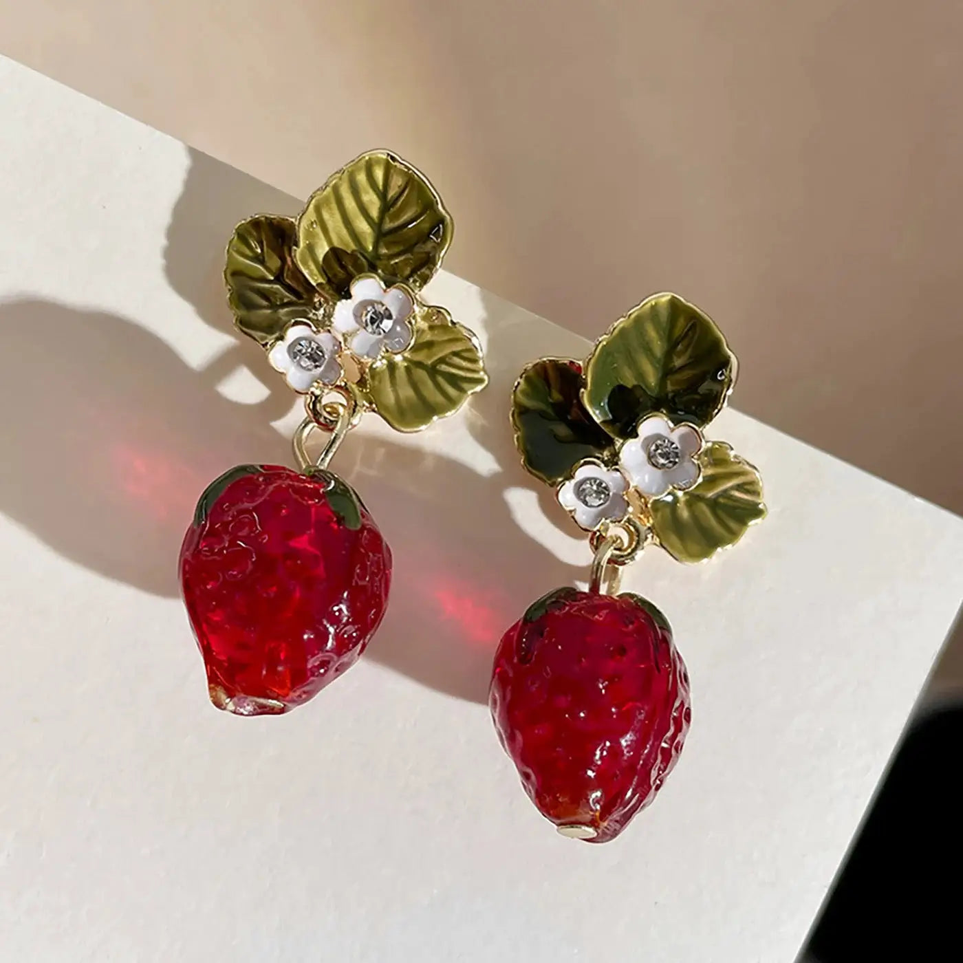 Pair of strawberry-drop earrings featuring gold-tone leaf tops, white flower accents, and rhinestone centers