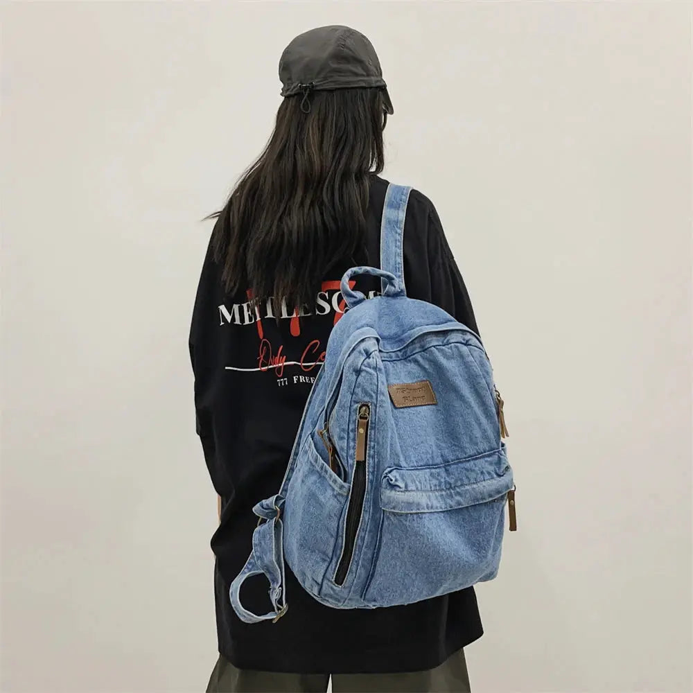Denim backpack with multiple pockets and front zipper, blue jean rucksack worn by person in a black tee