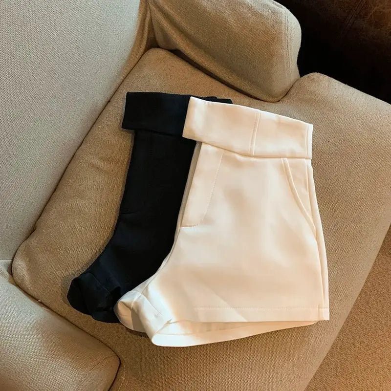 Women's high-waisted shorts set in black and white, two-piece, folded on a beige sofa.
