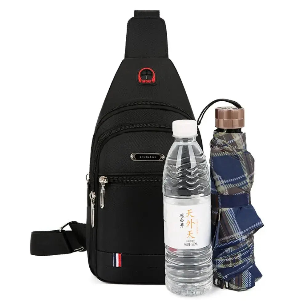 Black Oxford cloth men's messenger bag with three-zip pockets and crossbody strap, shown with bottle and umbrella.