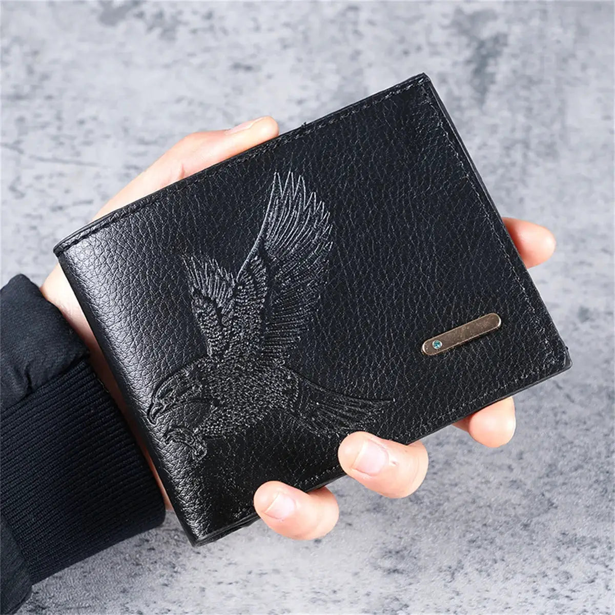 Black leather slim men's wallet with embossed eagle pattern, held in hand.