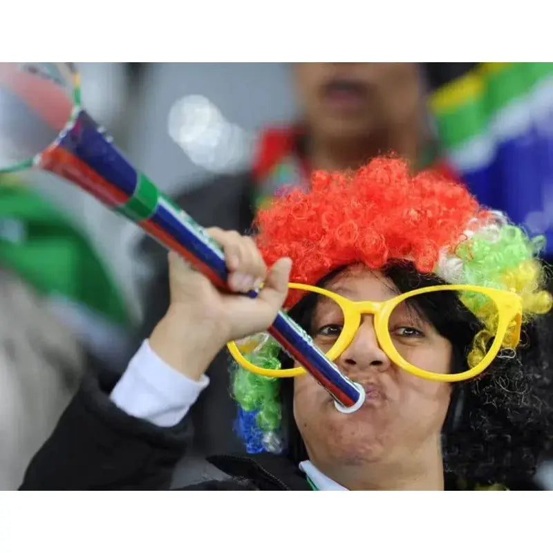Colorful clown wig with red, orange, green and yellow sections, worn with oversized yellow glasses and a party horn.
