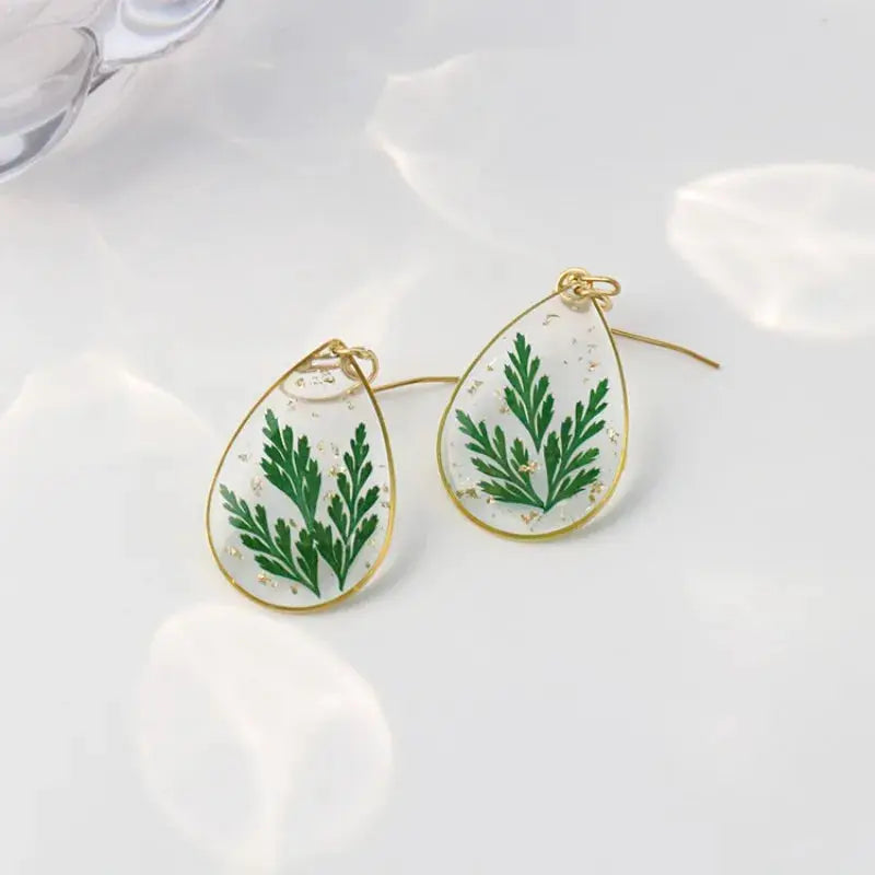 Pair of teardrop epoxy resin earrings with pressed green fern leaves and gold-tone frame
