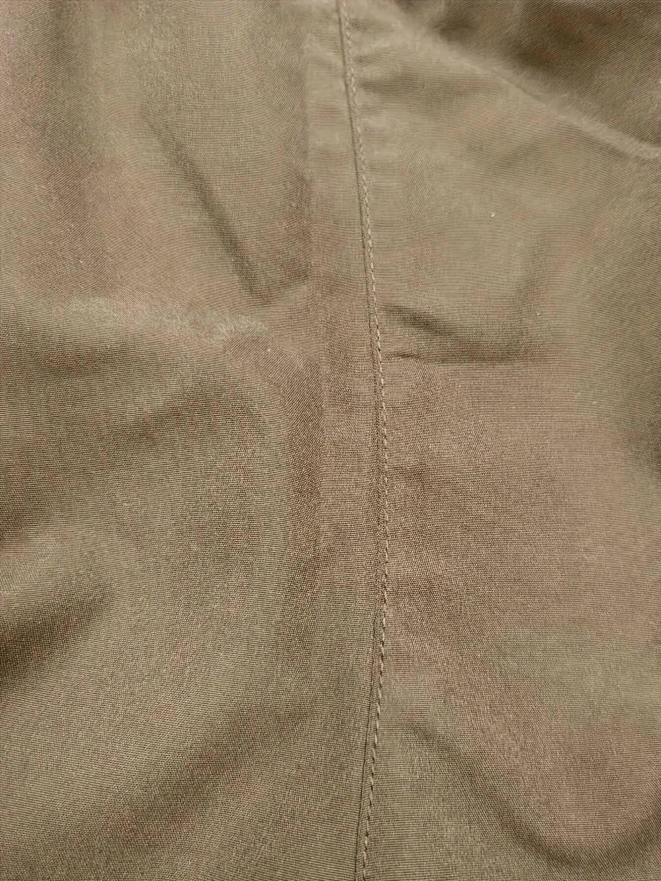 Men's cargo pants fabric close-up in tan khaki with visible center seam.
