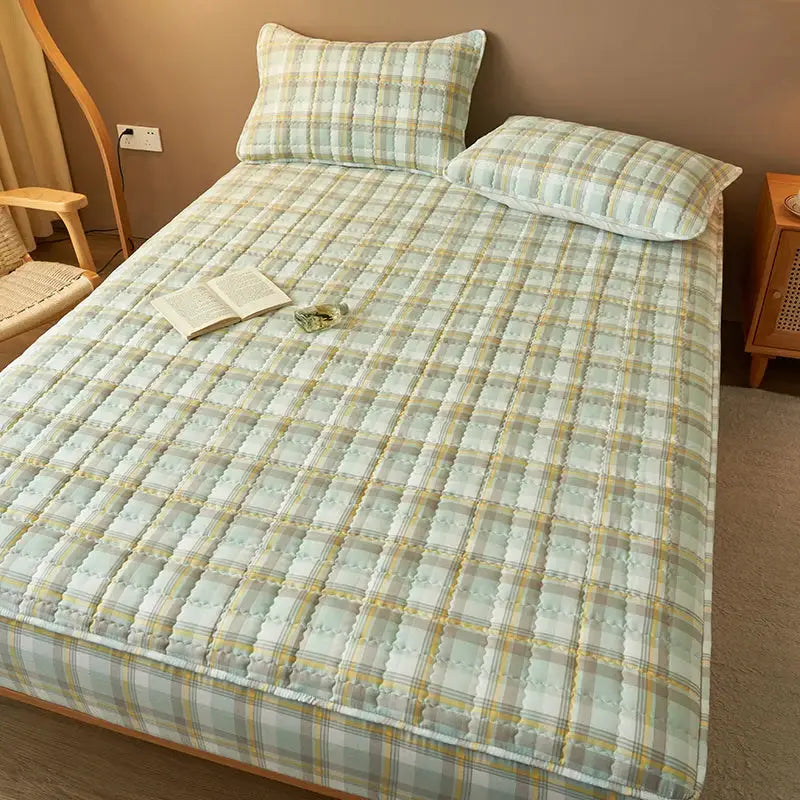 Simples Market quilted plaid mattress cover/protector with antibacterial, breathable fabric; two matching pillows on bed.