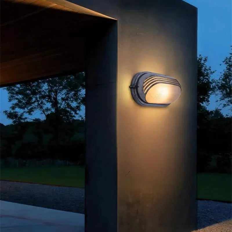 Outdoor retro LED wall lamp in dark metal with glass diffuser mounted on a pillar.