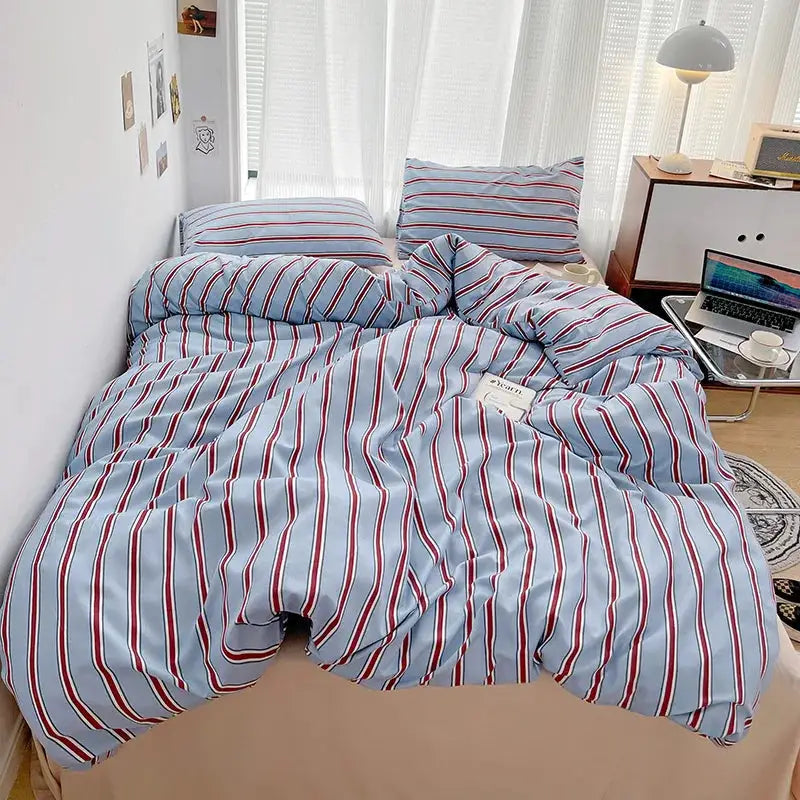 Duvet cover and four-piece sheet set in red and blue striped washed cotton on bed