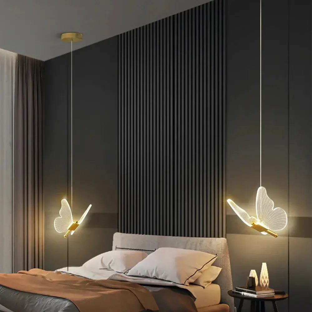 LED modern butterfly pendant lights by Simples Market, with gold accents, two hanging over a bed in a dark bedroom.