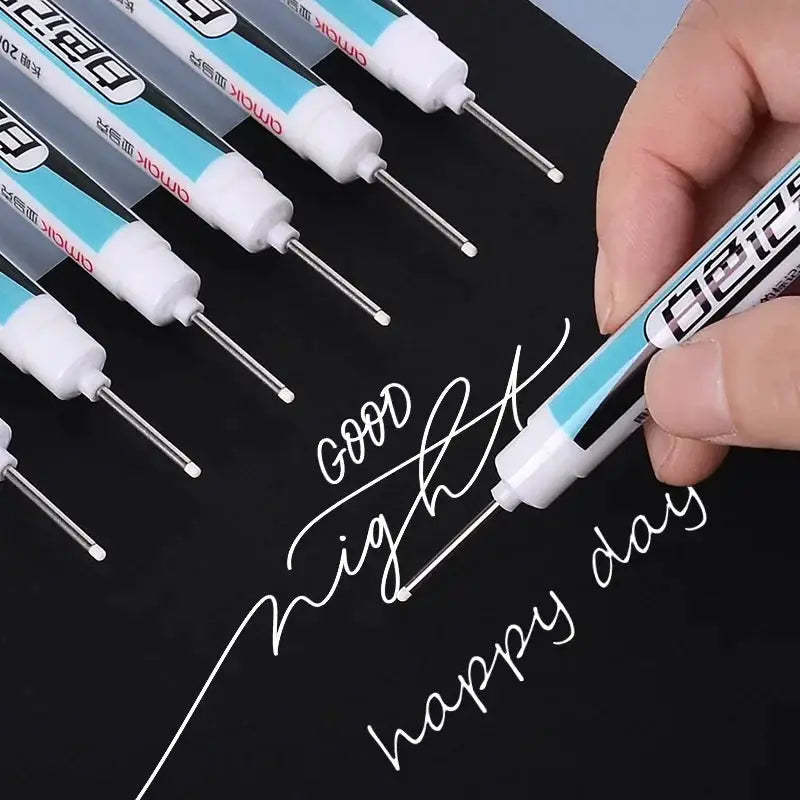 Simples Market white marker pens set; 0.7/1.0/2.5mm waterproof oil-based; six pens shown with one in use writing on black surface.
