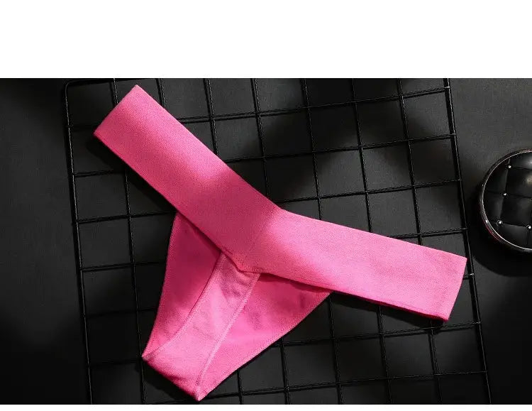 Pink women's thong underwear with wide elastic waistband, shown flat on a black grid background, vivid fabric.