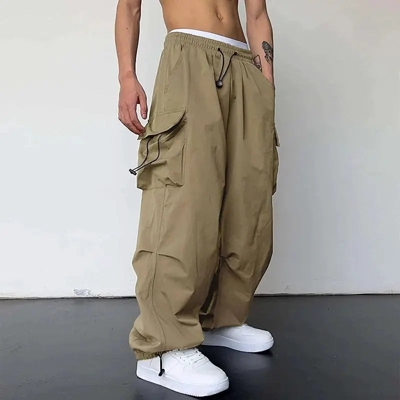 Men's cargo pants in tan khaki with drawstring waist, oversized wide-leg fit and large side cargo pockets.