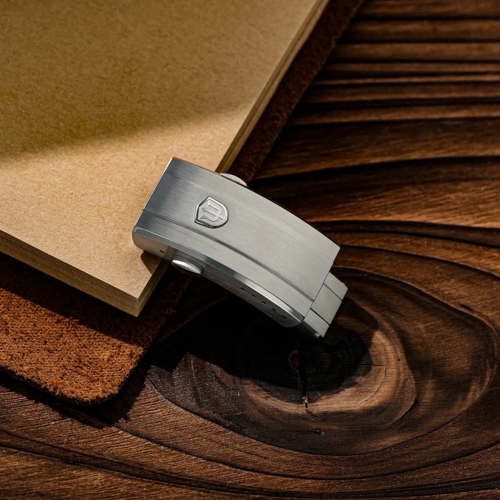 Stainless steel watch clasp with Watchdives shield logo on a wooden surface