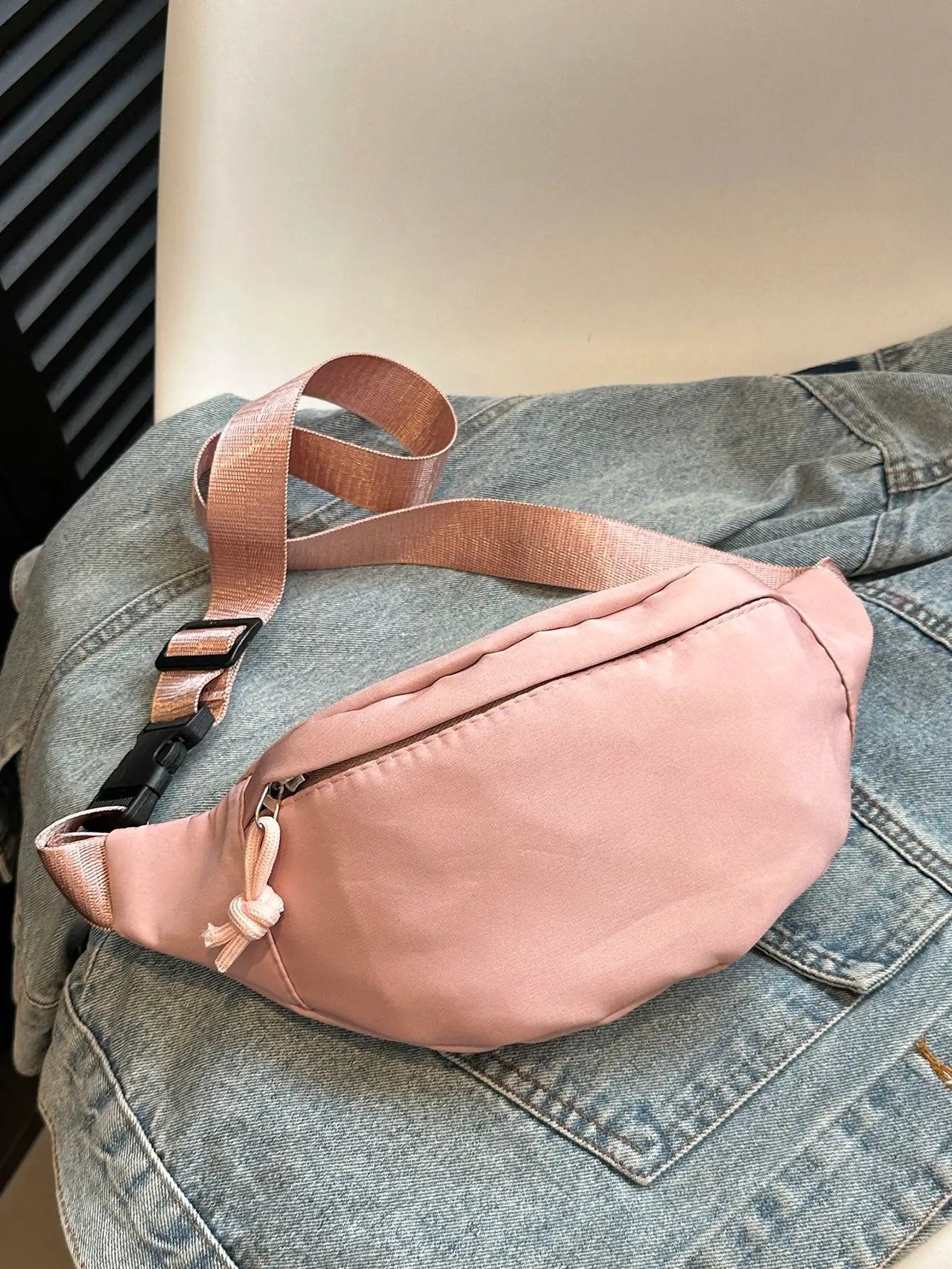 Fanny pack waist bag in pink with adjustable strap, crossbody style, on denim.