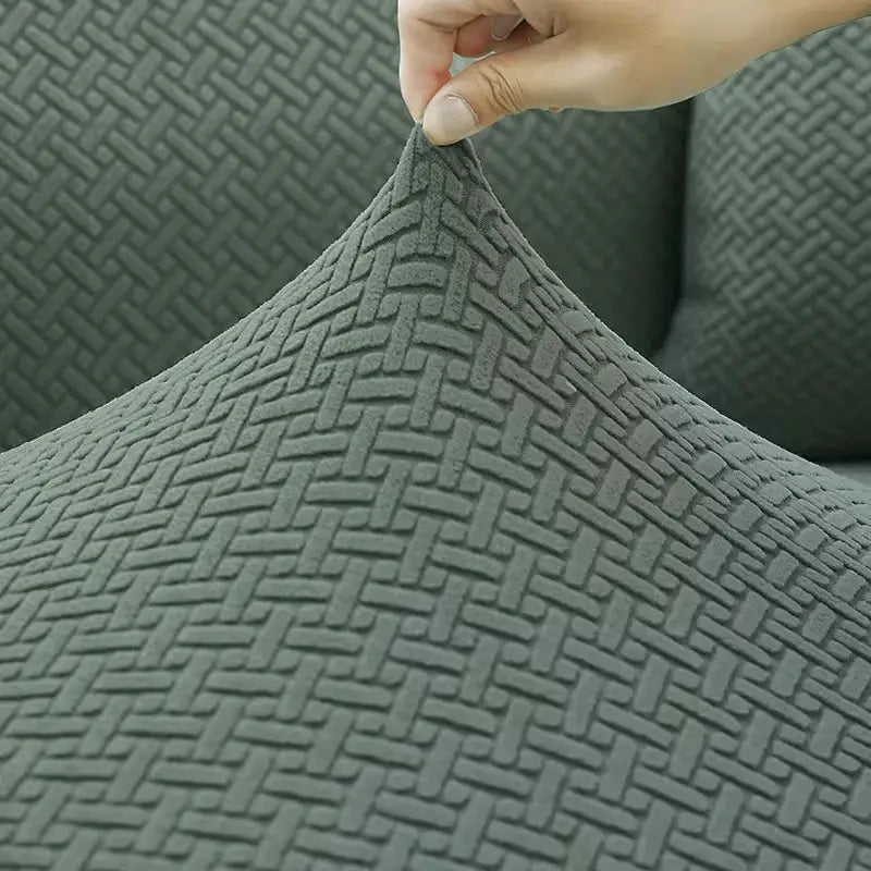 Jacquard sofa cover, grey elastic thick fabric with a woven pattern, shown stretching over a corner sofa.