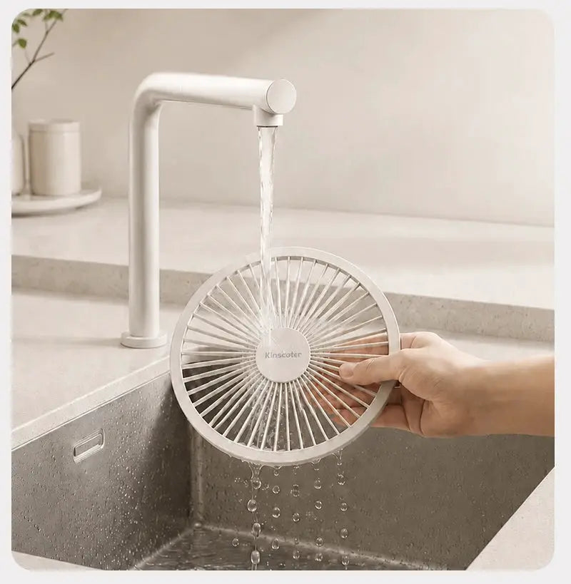 Kinscoter white circular desk fan with radial grill being rinsed under running water at a kitchen sink