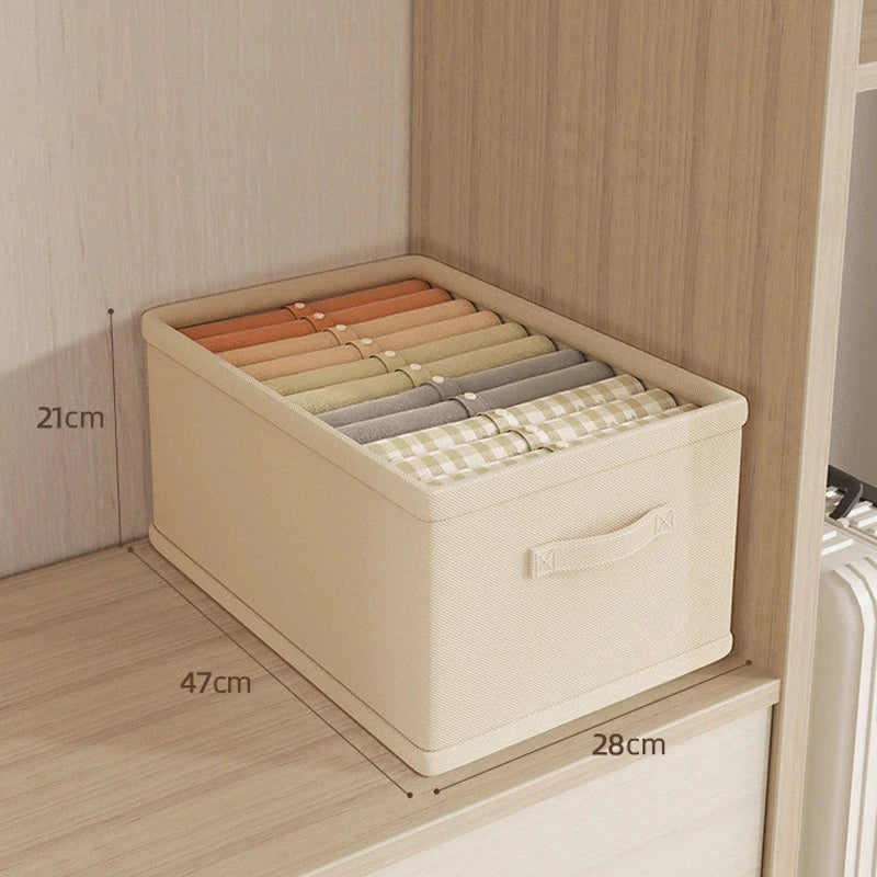Beige fabric clothes organizer box with side handle, filled with folded trousers, underwear and socks on wardrobe shelf