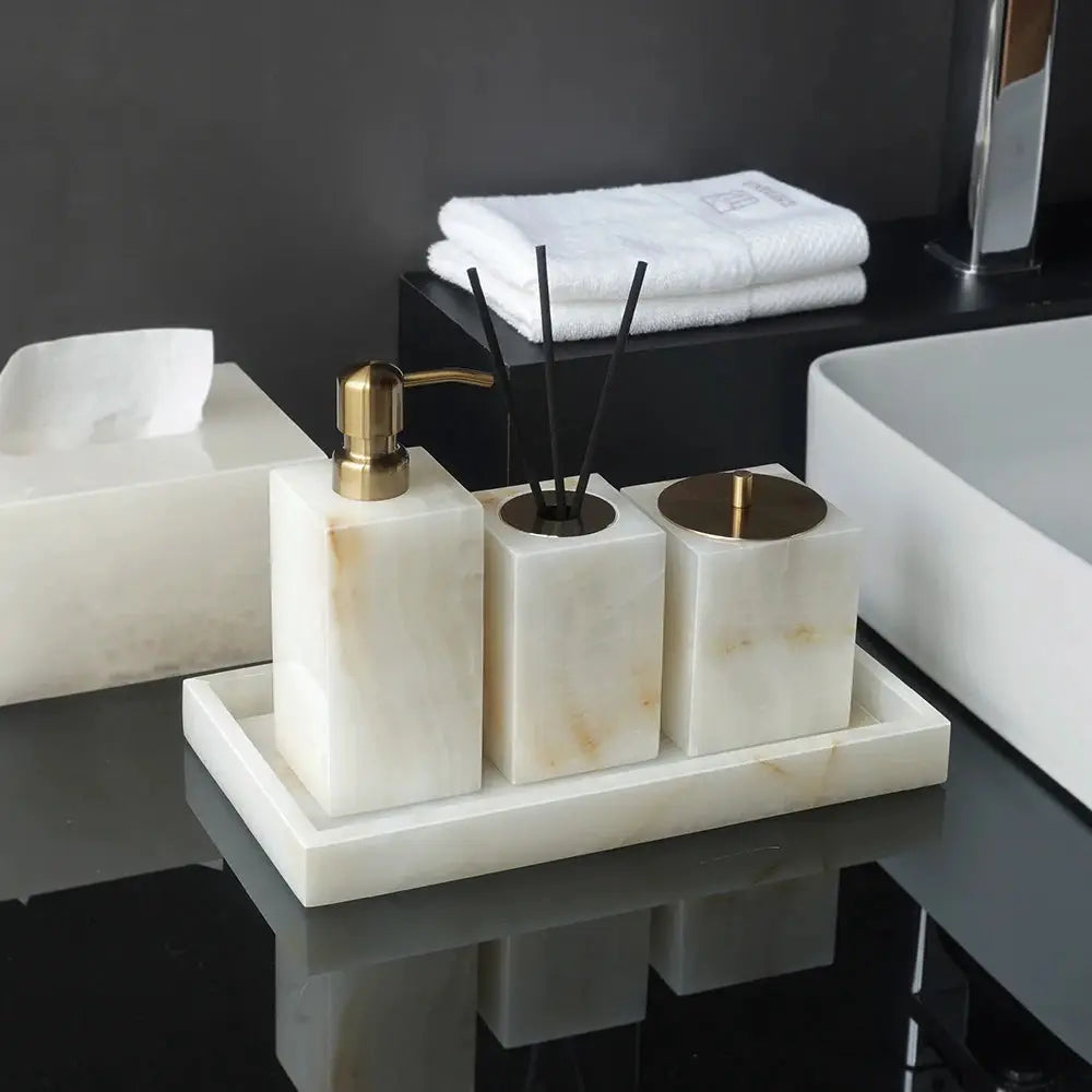 Three-piece white onyx marble bathroom accessories set with soap dispenser, reed diffuser, and storage jar on a tray