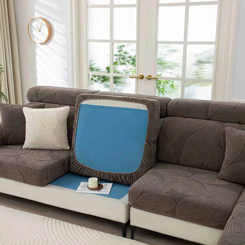Thick plush sofa cushion cover in blue with elastic edges on a brown leaf-patterned sofa