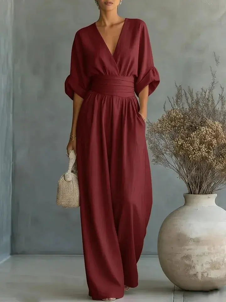Simples Market waist V-neck jumpsuit in wine red; wide-leg, mid-sleeve with wide belt, modeled with woven bag