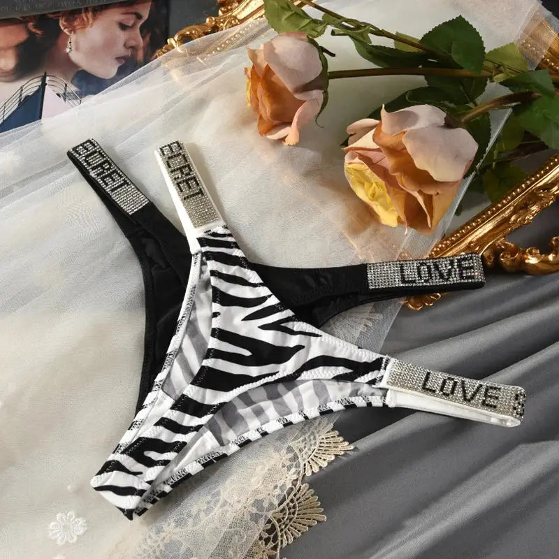 Two low-rise zebra-print thong panties with rhinestone LOVE straps (black and white)
