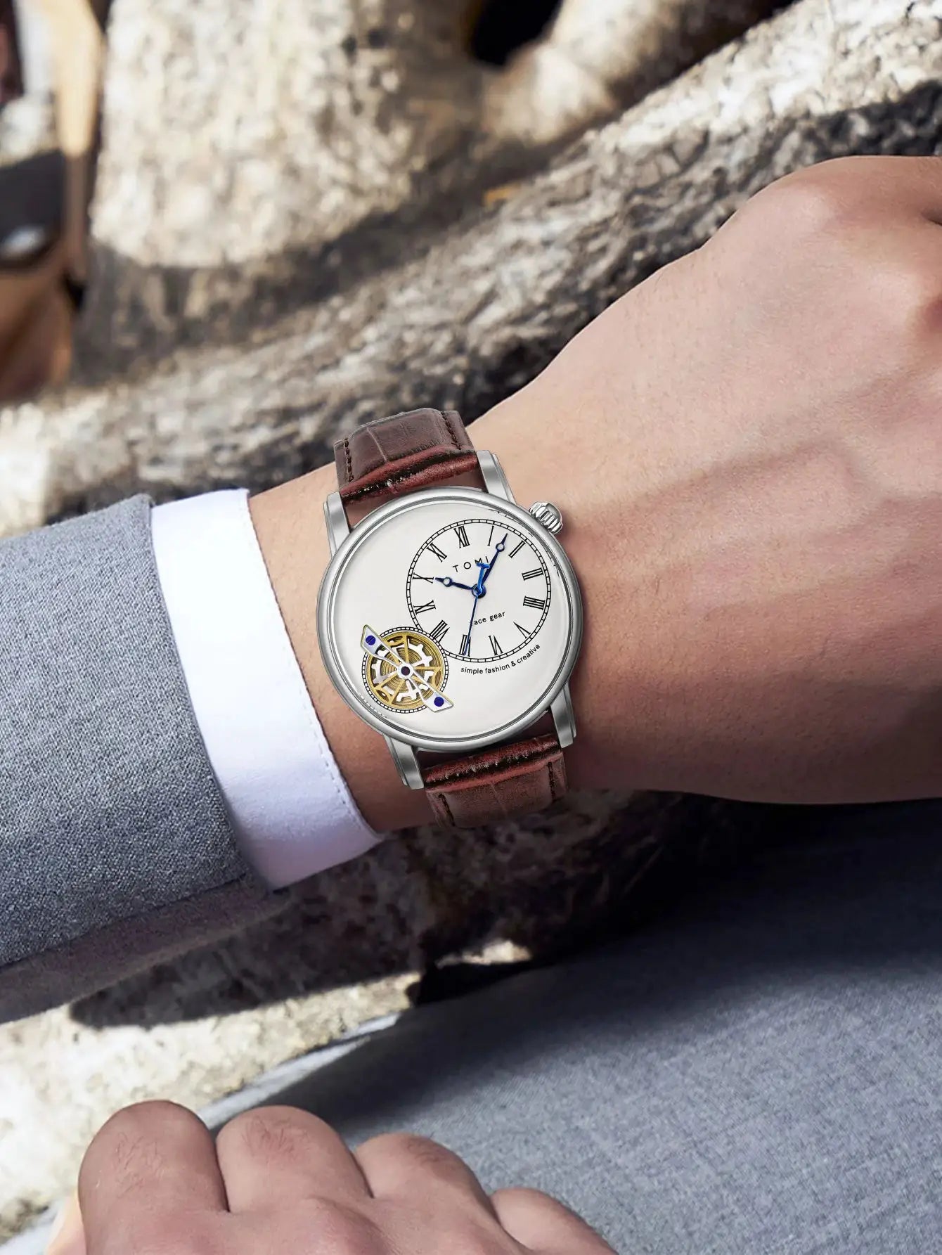 TOMI men's wristwatch with brown leather strap, silver case, white dial, Roman numerals, blue hands, and visible gears.