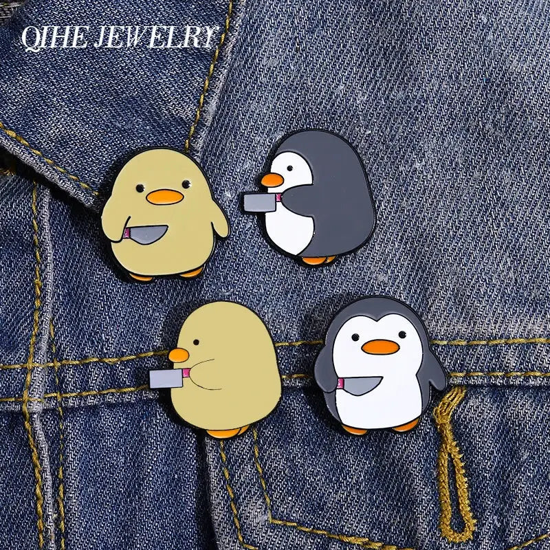 Four cartoon penguin enamel pins on denim; beige, gray, and white birds with orange beaks.