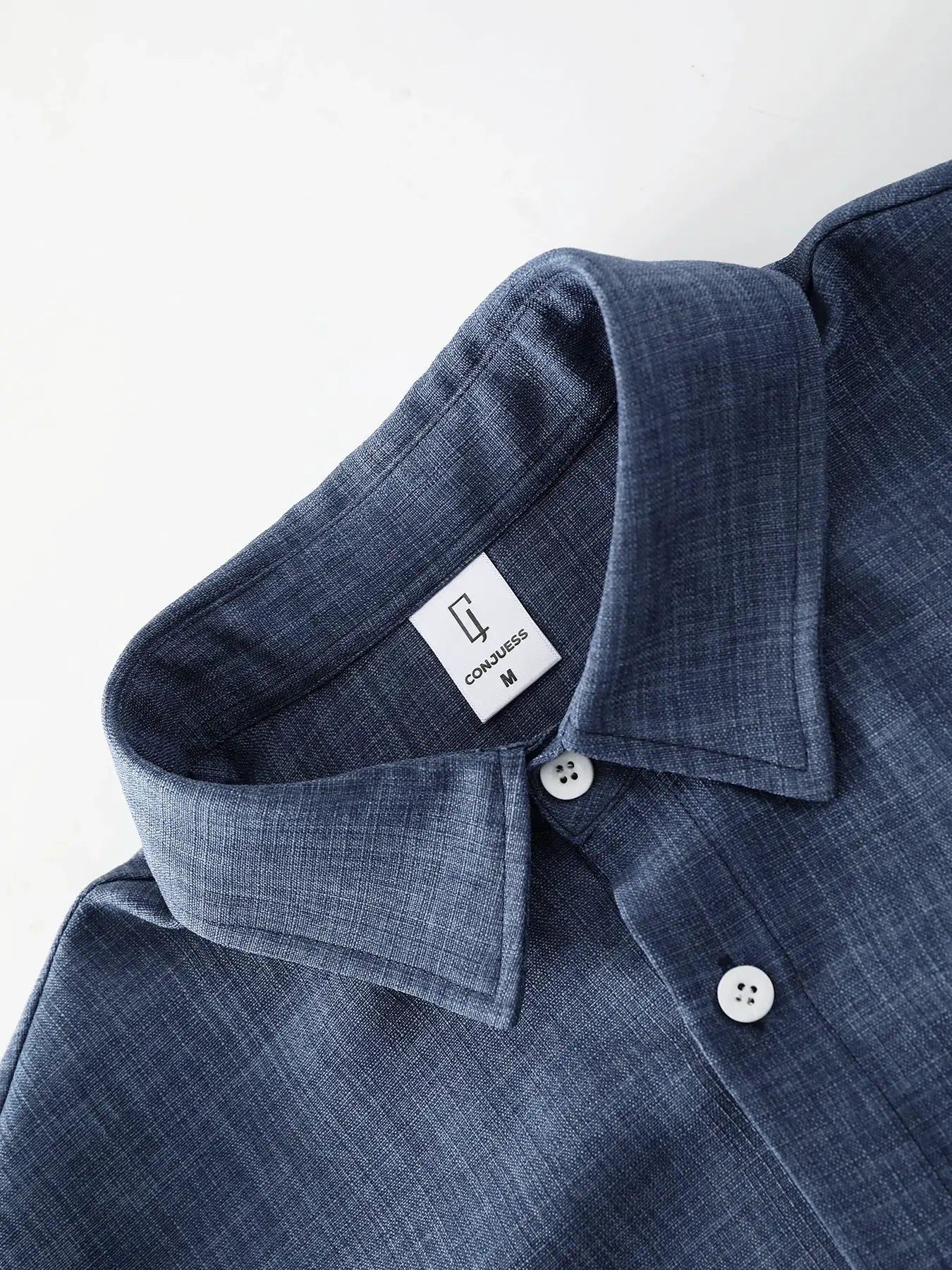 Men's blue linen shirt collar close-up with white buttons and Conjess tag size M