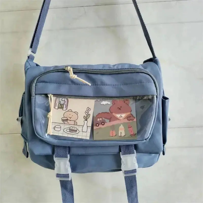 Blue canvas crossbody bag with front zip pocket and two cartoon patches; adjustable strap.