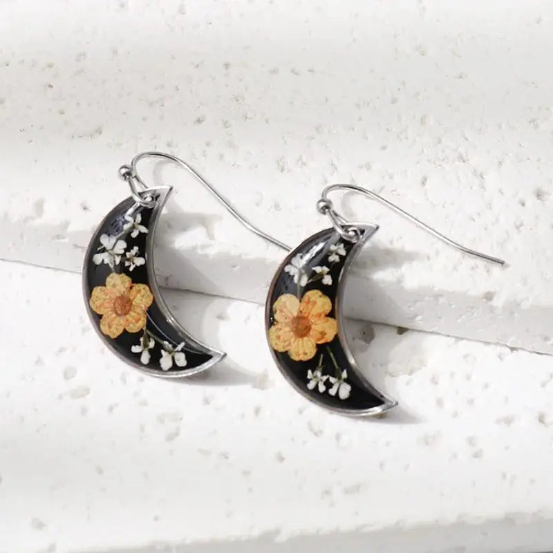 Pair of crescent moon epoxy resin earrings with pressed orange flowers and white buds on black background, silver hooks