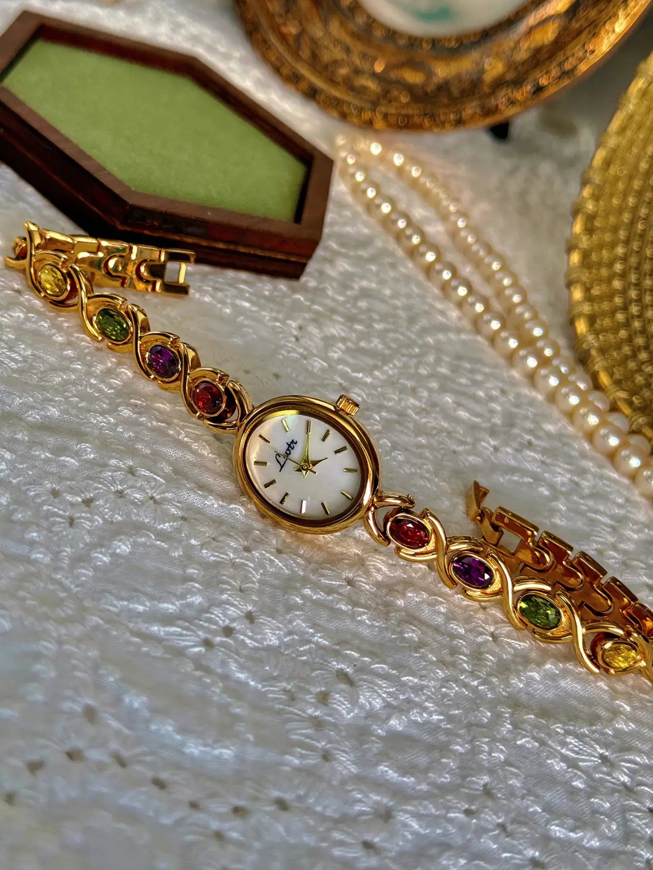 Gold-tone luxury women's watch by Simples Market with colorful gemstone inlays and an oval mother-of-pearl dial.